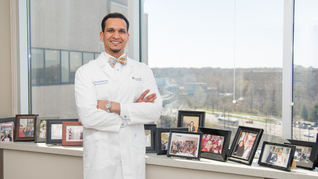 Dr. Karim Qumosani stands in his office among photos of family, team members, and patients.