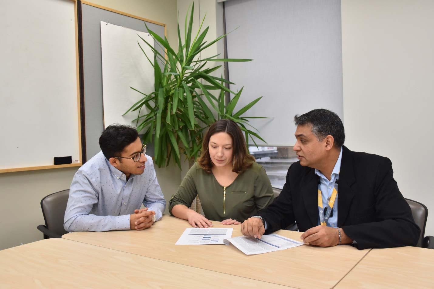 Jayneel Limbachia, Emily Ionson and Dr. Akysha Vasudev sitting together at a table and looking at papers.