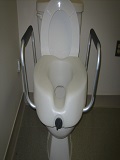Image shows a standard raised toilet seat with metal arms to provide stability when sitting/standing to use toilet.