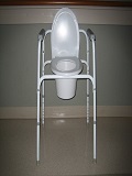 Image shows a standard Commode Chair with adjustable height and build in handle supports for stability.