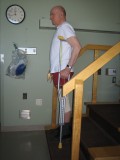 Image of a man demonstrating how to go down the stairs with one crutch and using a railing