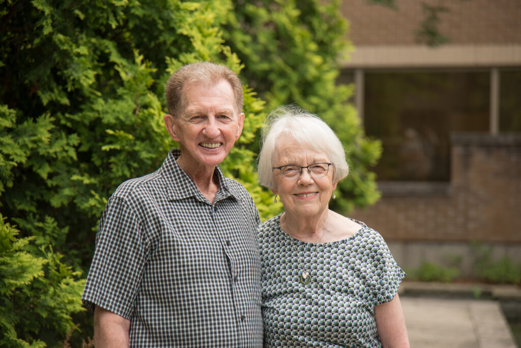 Dave and Sharon Gast stand next to each other smiling in an outdoor garden space.