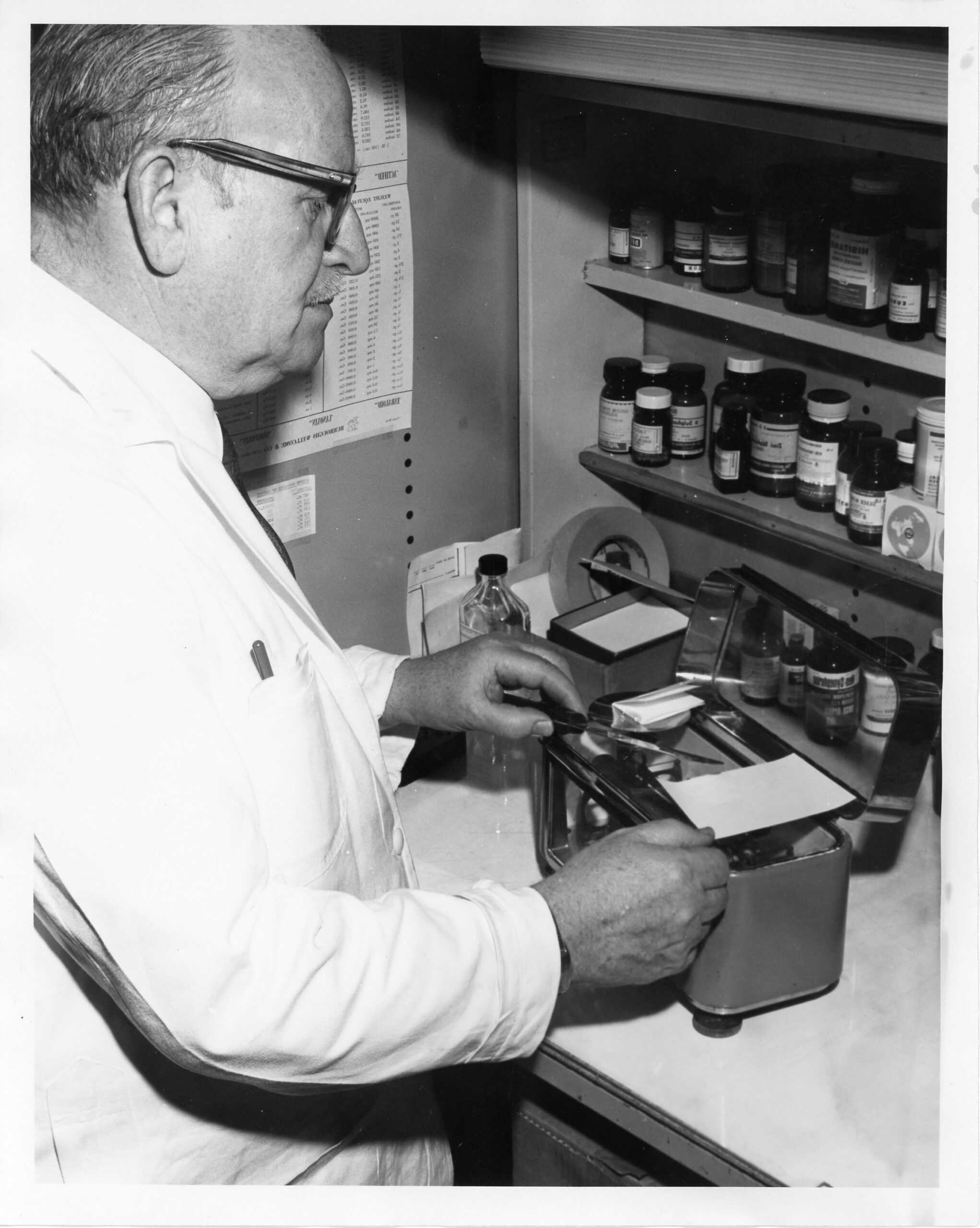 Head Pharmacist Fraser Stewart (circa 1958) using a torsion balance scale to measure out a powder to be wrapped into the powder paper on the right-hand side of the scale. It wasn't until a decade later most medications became available as tablets or capsules.