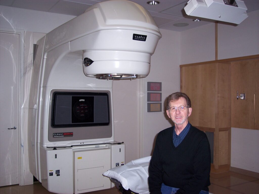 Dave Gast sits in a treatment room in front of radiation equipment.