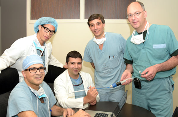 Five male doctors in scrubs sitting around a laptop and holding a small patient implant device.
