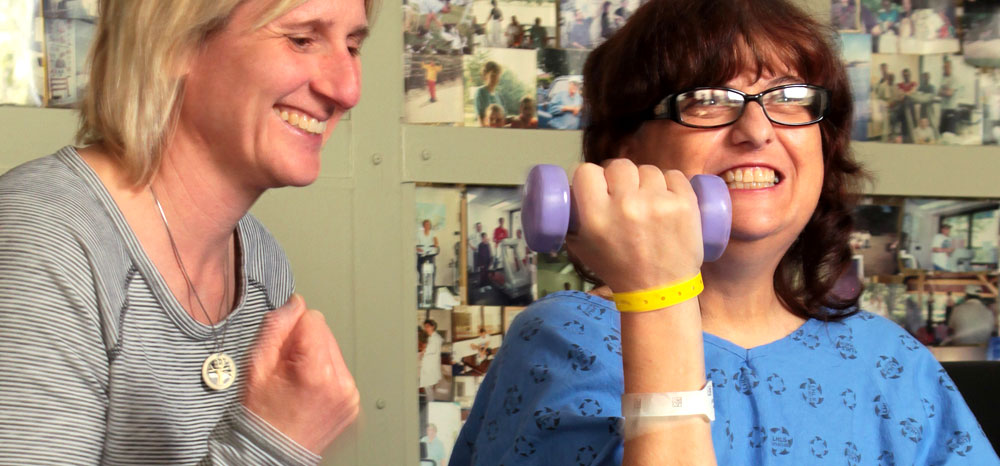 Female physiotherapist assisting female patient lifting small weight in an upward motion.