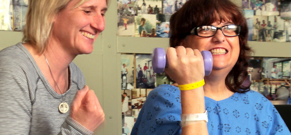 Female physiotherapist assisting female patient lifting small weight in an upward motion.