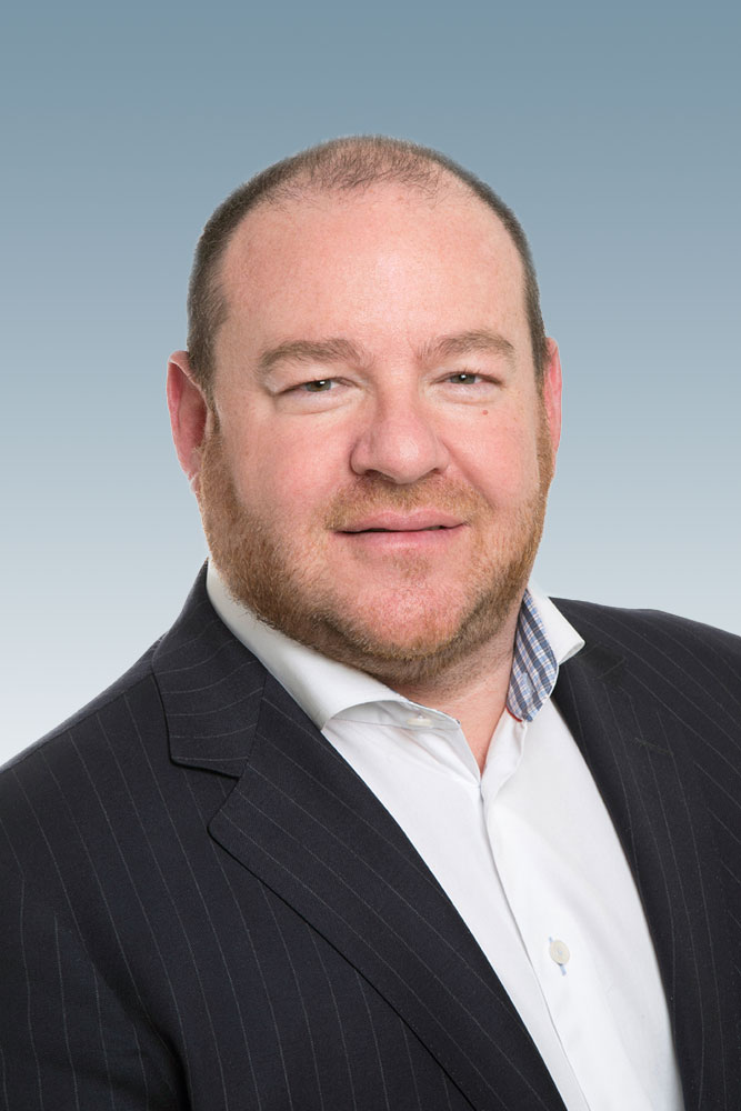 Professional headshot of a man wearing a white dress shirt and black blazer, smiling at the camera.