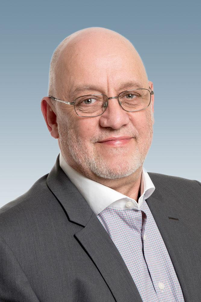 Professional headshot of a man wearing a white dress shirt and grey blazer, smiling at the camera.