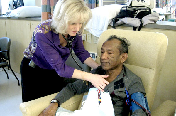 Female nurse with blonde hair assisting a gentleman patient at a dialysis chair.