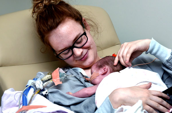 Young mother wearing glasses holding her newborn baby in a reclined hospital chair shortly after birth.
