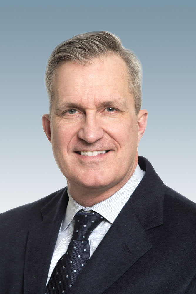 Professional headshot of a man wearing a white dress shirt, polka dot tie, and black blazer, smiling at the camera.