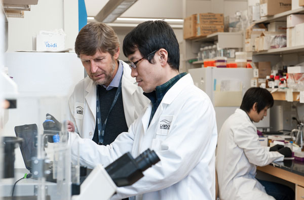 Two middle aged males in lab coats looking at a beaker in a lab setting