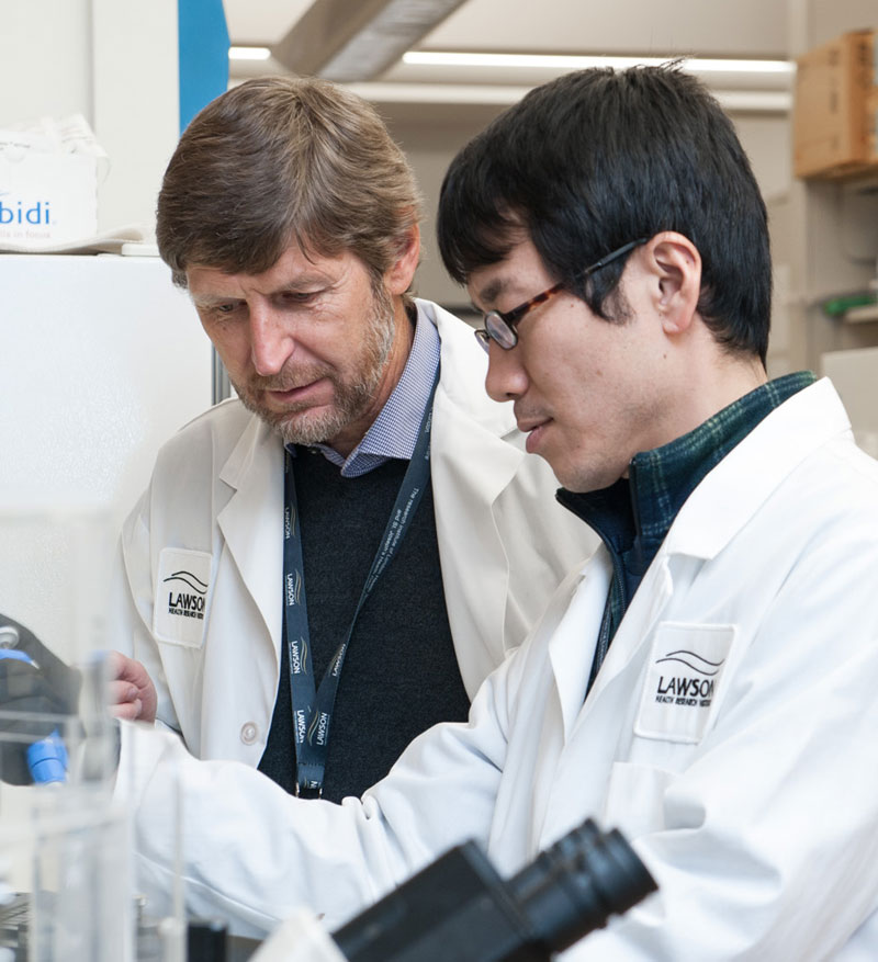 Two males in lab coats looking at a beaker in a lab setting.