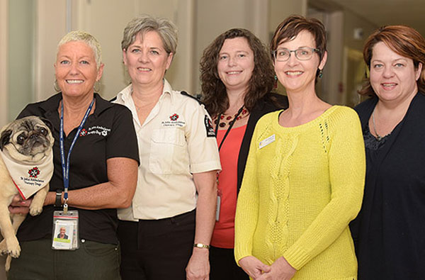 Five female hospital staff members dressed in casual work clothes smiling while holding a pug breed dog.