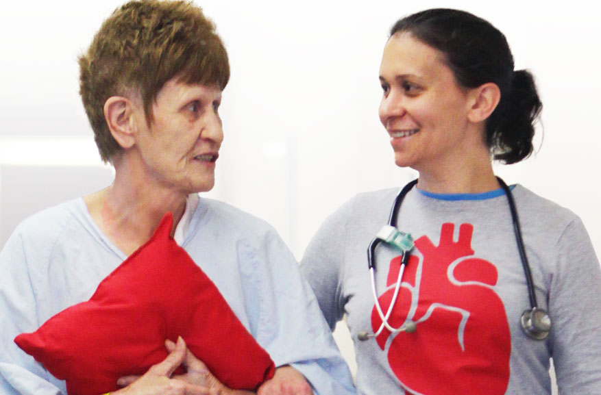 Female nurse smiling while walking with elderly woman patient together down a hallway at the hospital.