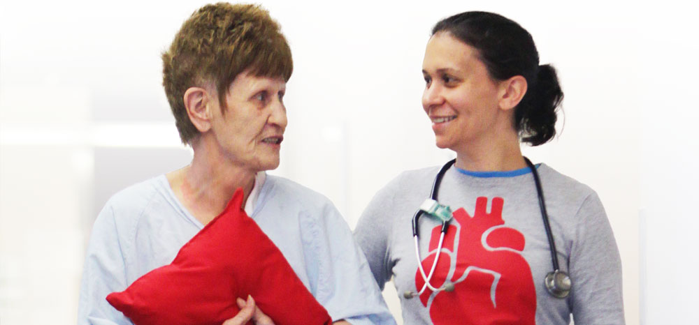 Female nurse smiling while walking with elderly woman patient together down a hallway at the hospital.