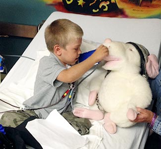 A young boy using medical instruments on stuffed animal while in hospital bed.