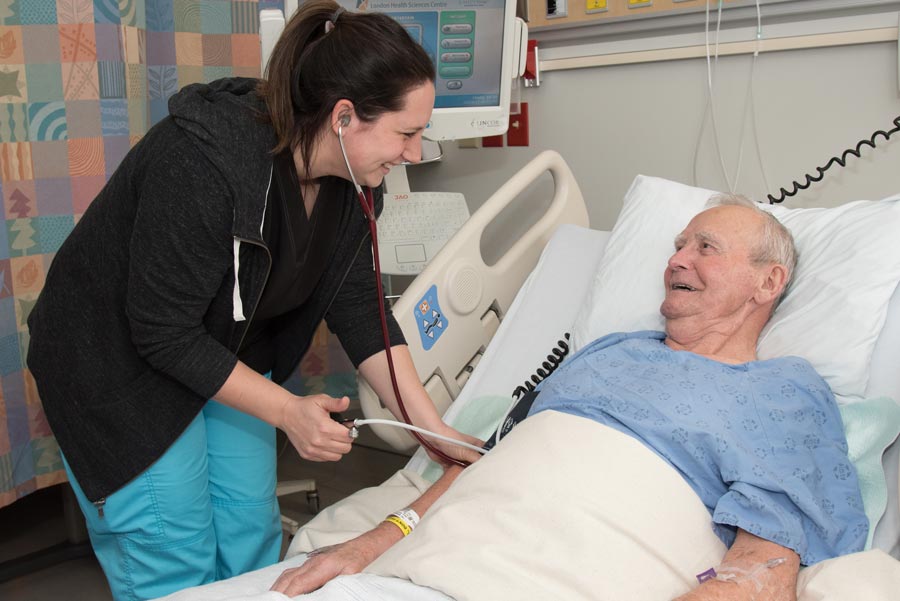 Female nurse taking blood pressure at the bedside of male patient in hospital room. 