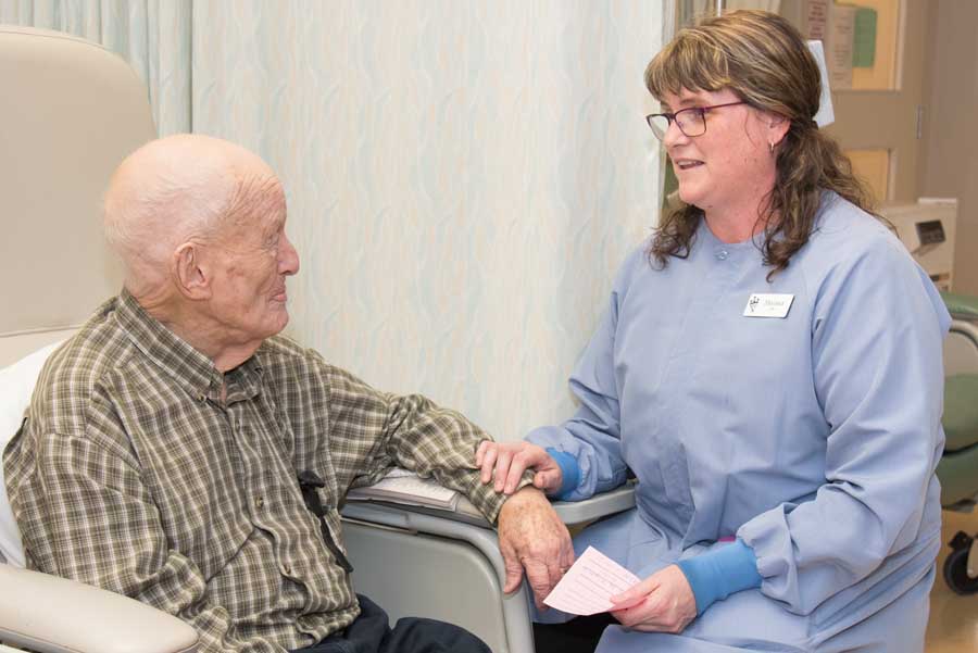 Female nurse sitting beside a male patient talking while holding a small piece of paper.