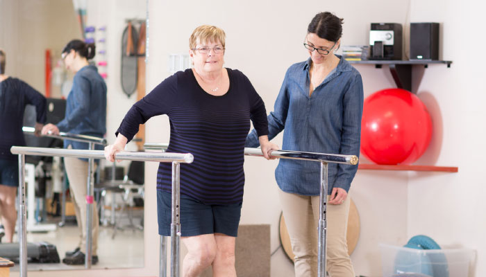 Woman pictured using rehabilitation walking rails with a medical professional by her side.