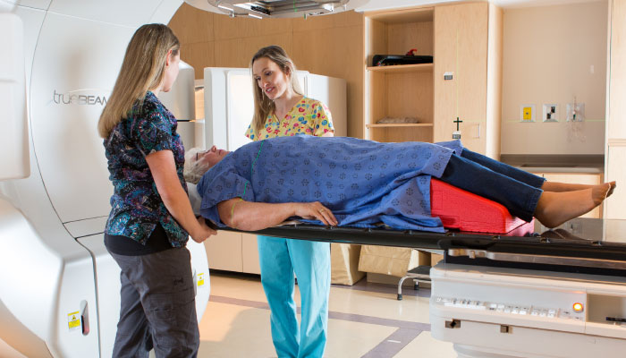 Two female nurses pictured treating a patient with a radiotherapy system.
