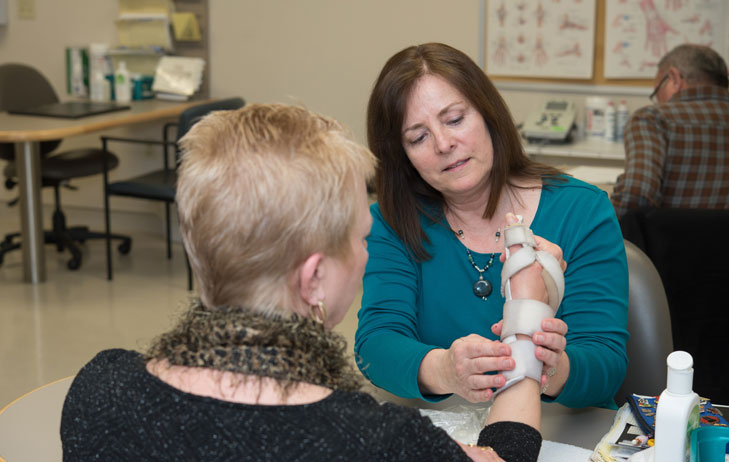 A seated medical professional helping a patient with a hand brace. 