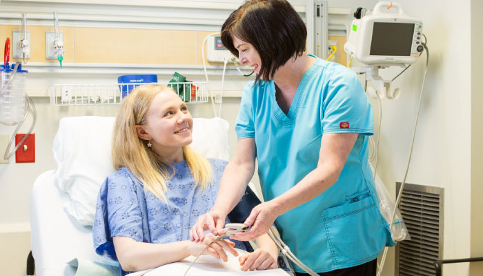 Medical professional pictured using a pulse oximeter on a young patient in a hospital bed.