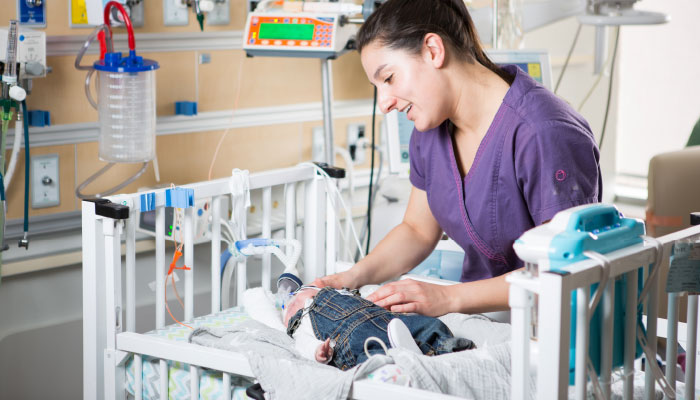 Nurse pictured caring for a newborn baby in a paediatric crib.