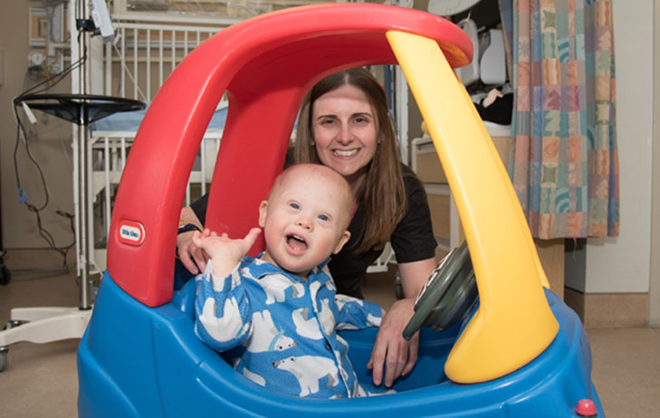 Mother pictured smiling with son playing in a toy car. 