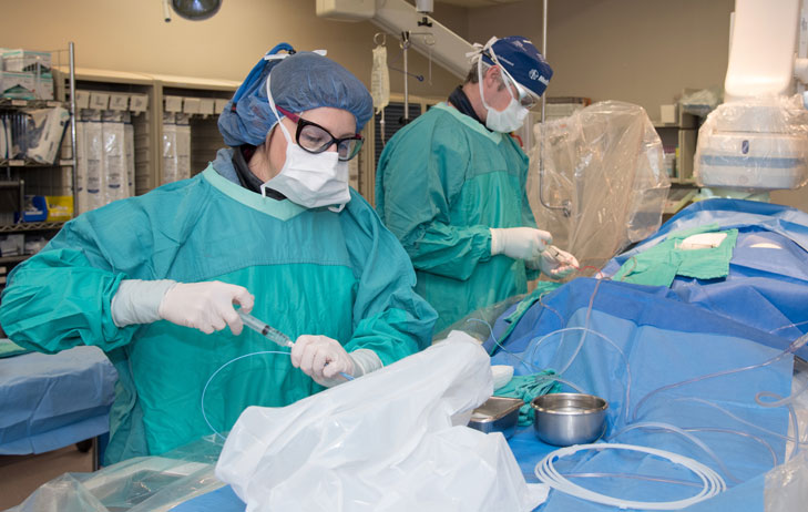 Two doctors pictured in scrubs preforming a medical procedure.