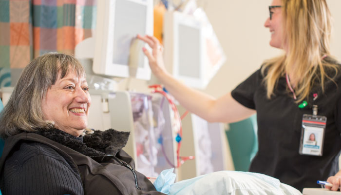 Patient in hospital bed pictured smiling with medical professional beside her.