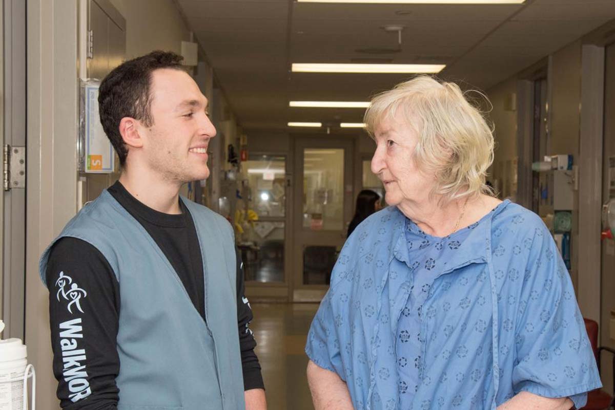 LHSC staff member and a patient in a hospital gown talking in a hallway. 