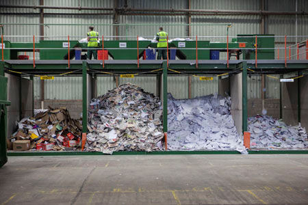 Photograph of manual sorting stations for incoming recyclable material with large bunkers underneath that collect the sorted materials together.