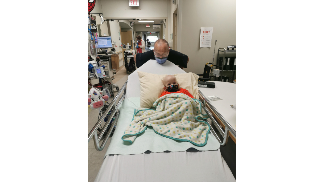 A healthcare professional pushes a small child on a hospital bed.