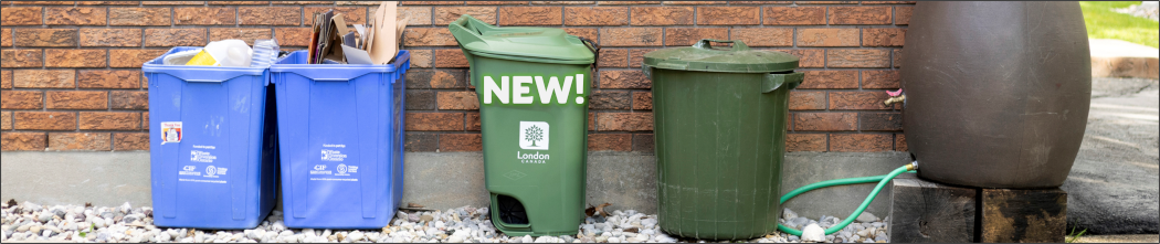 Photograph of two blue recycling containers, the new London Green Bin, a trash bin, and rain water barrel at the side of a house.