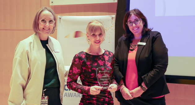people smile at camera while one holds an award