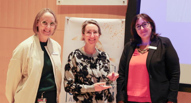People stand smiling at camera while one in middle holds an award