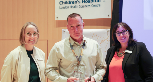 people stand smiling at camera while one in middle holds an award