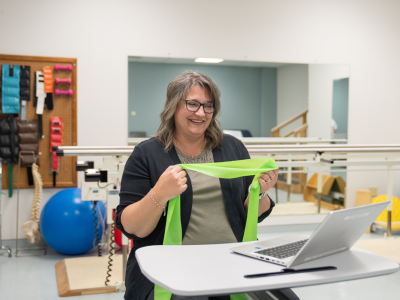 Patrice using green theraband to demonstrate exercises in front of laptop 