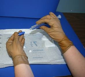 Gloved hands holding sterile #22 safe step huber needle and flolink valve.