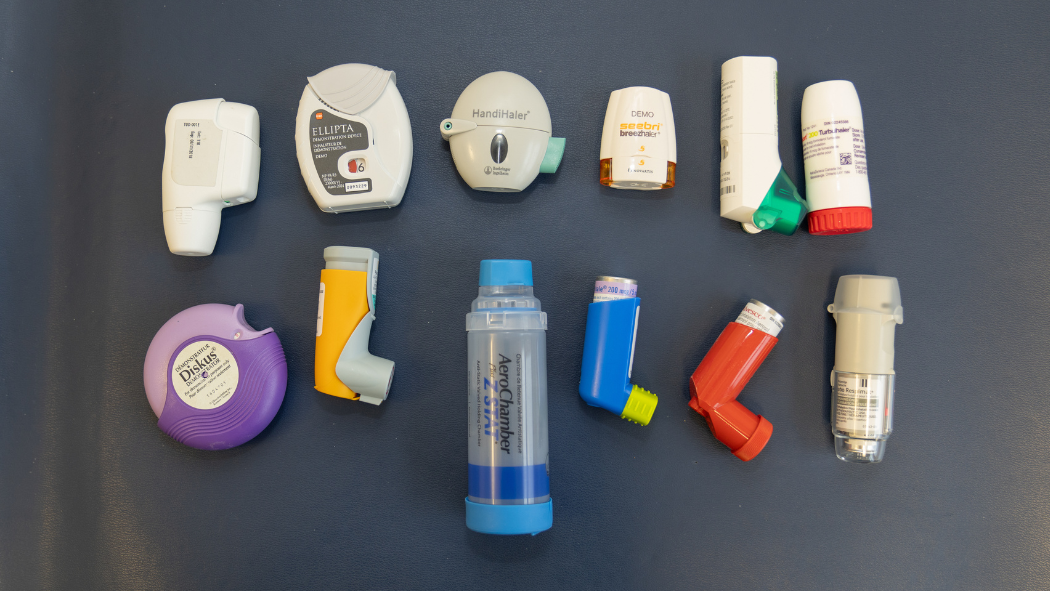 A variety of inhalers, including dry powder and metered dose types, are arranged on a flat dark surface.