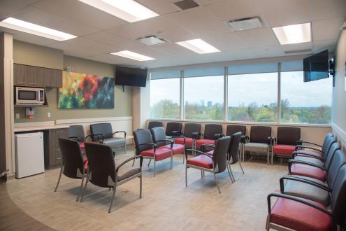 a lounge room with many seats, a small fridge, a microwave and two screens