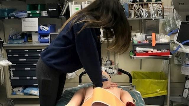 A high school student administering CPR to the trauma simulation mannequin after applying a pelvic binder.