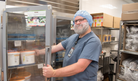 Food services worker smiles at camera while opening a fridge