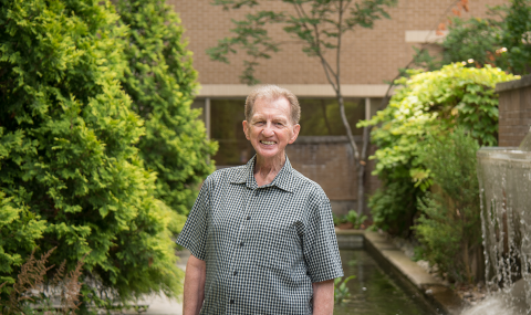 Dave Gast stands in a garden in front of a fountain