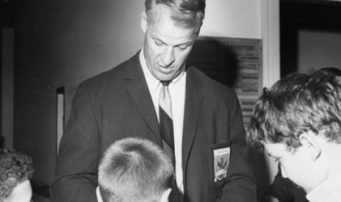 Black and white photo of hockey legend Gordie Howe signing hockey cards with three young patients