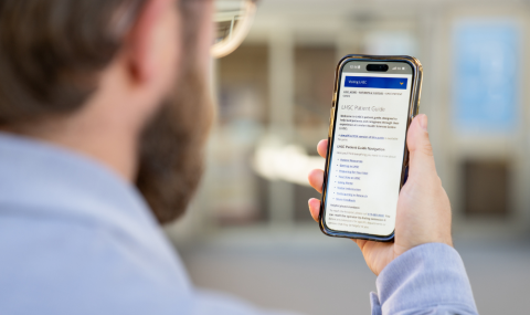A person holding a smartphone and viewing a webpage titled “LHSC Patient Guide” while standing outdoors.