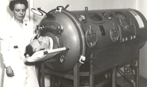 black and white photo of nurse standing beside patient in iron lung