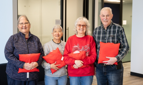 Image of four people standing side by side holding red pillows in both hands.